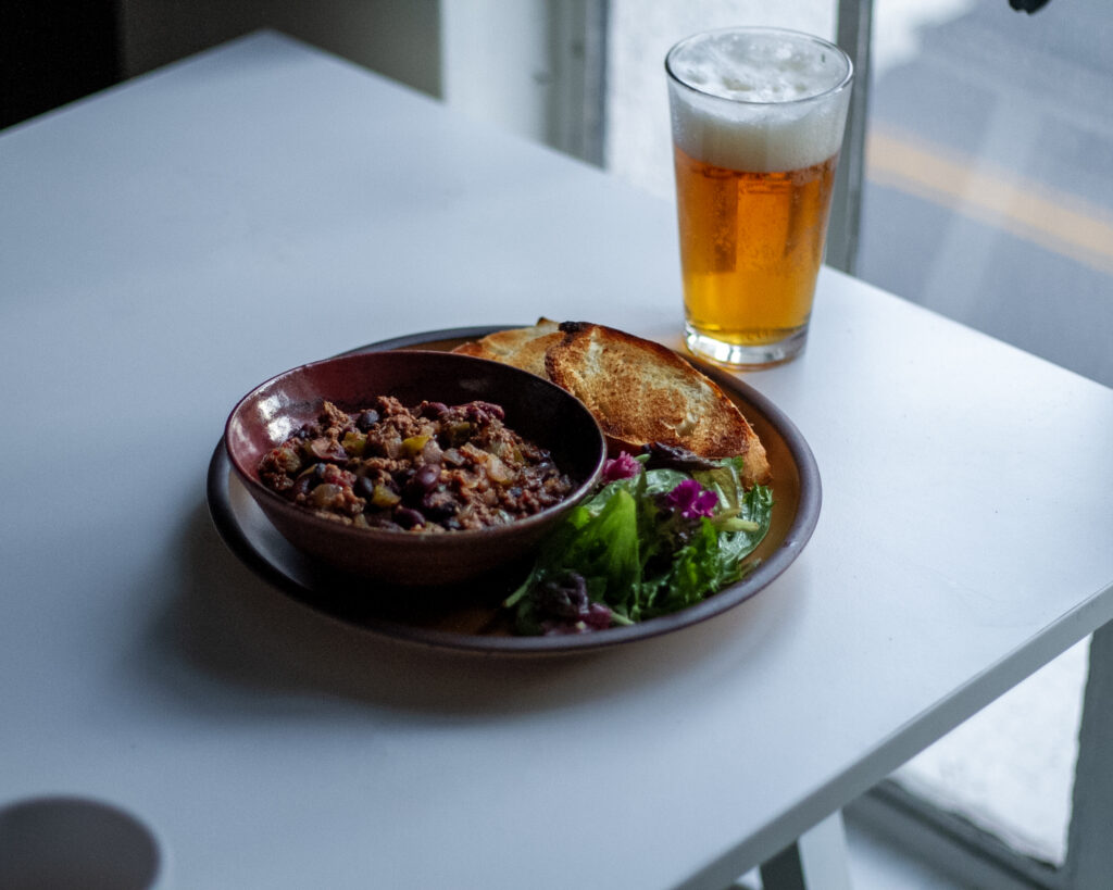 Ground beef chili with green salad, crusty bread, and foamy beer